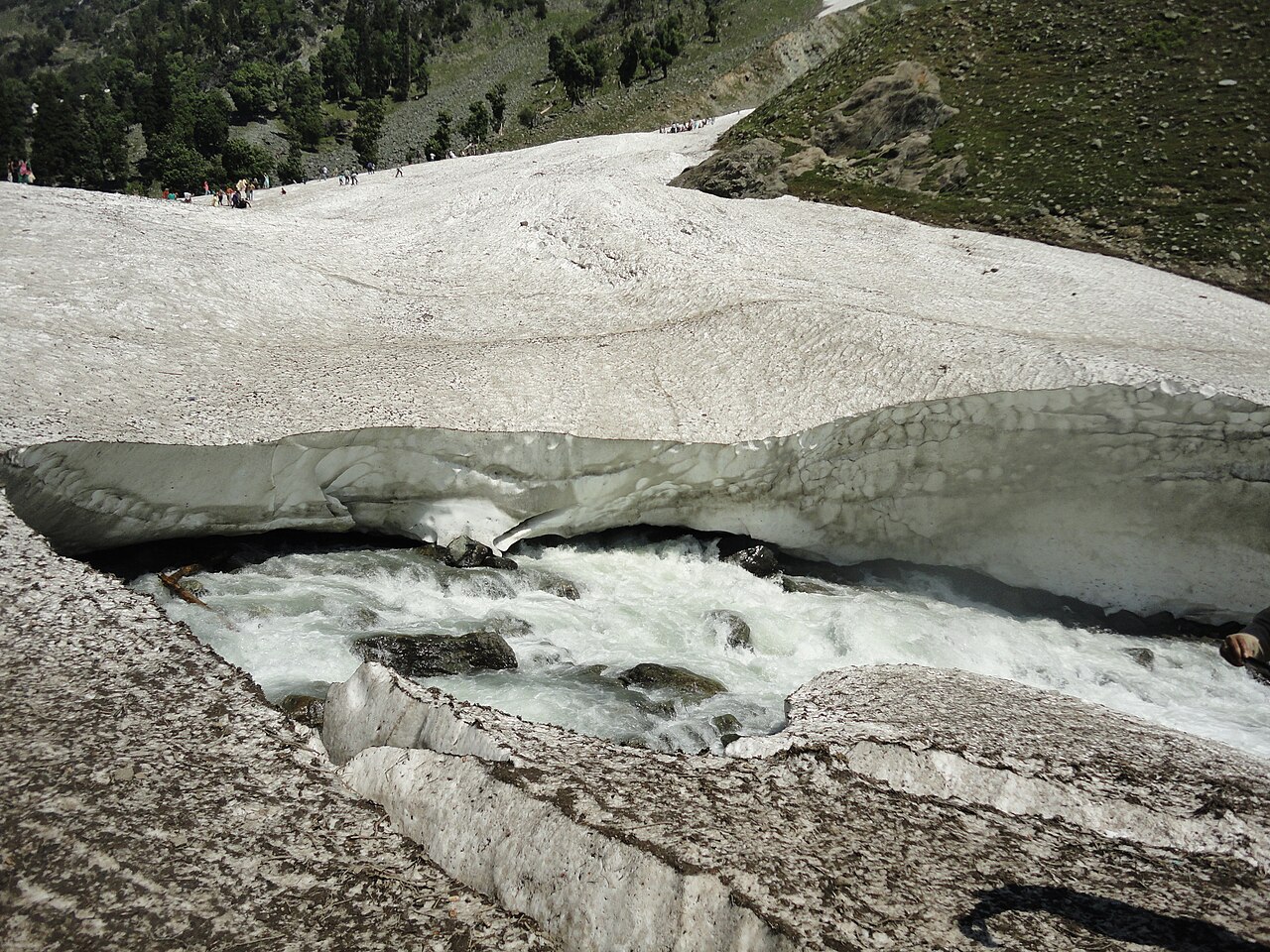 Fast-flowing stream cutting through rocky snow fields at Chandanwari