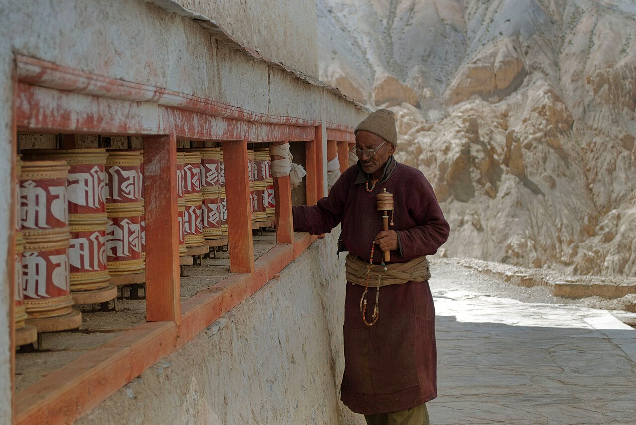 Large metal prayer wheels mounted along a whitewashed wall at Thiksey