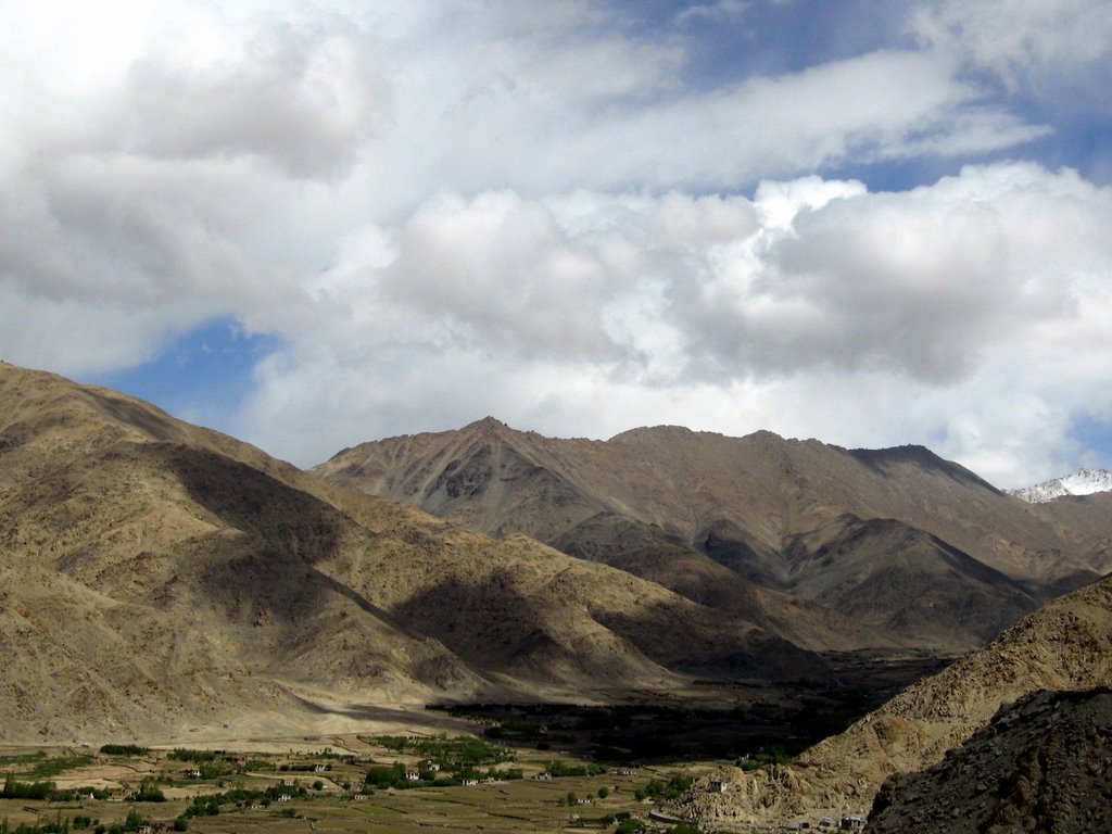 A green valley floor surrounded by massive, arid Himalayan mountains.