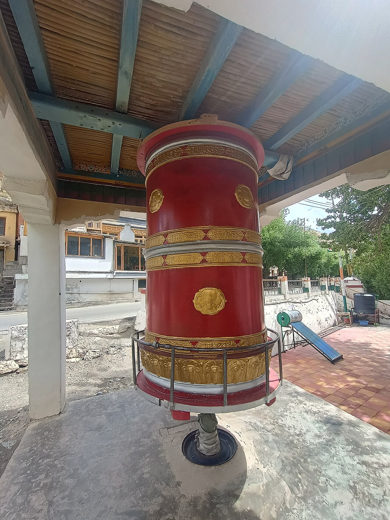 Row of large copper prayer wheels along an old stone monastery wall in Ladakh