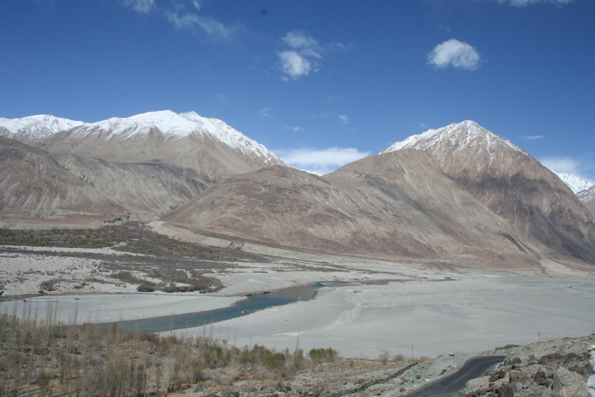A four-wheel-drive vehicle driving along a dusty mountain road near the Shyok River
