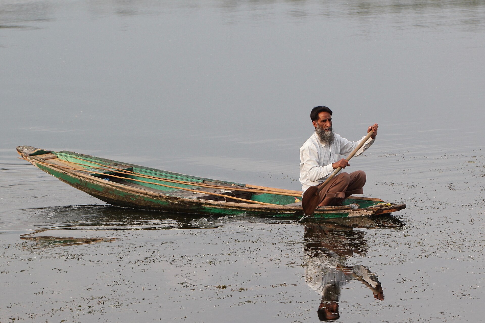 Local boatman rowing a shikara with mountains in background
