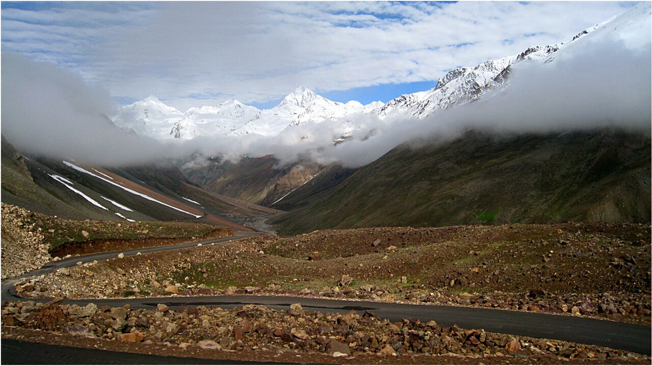 A clear, winding road cutting through dry brown mountains under a bright blue sky.