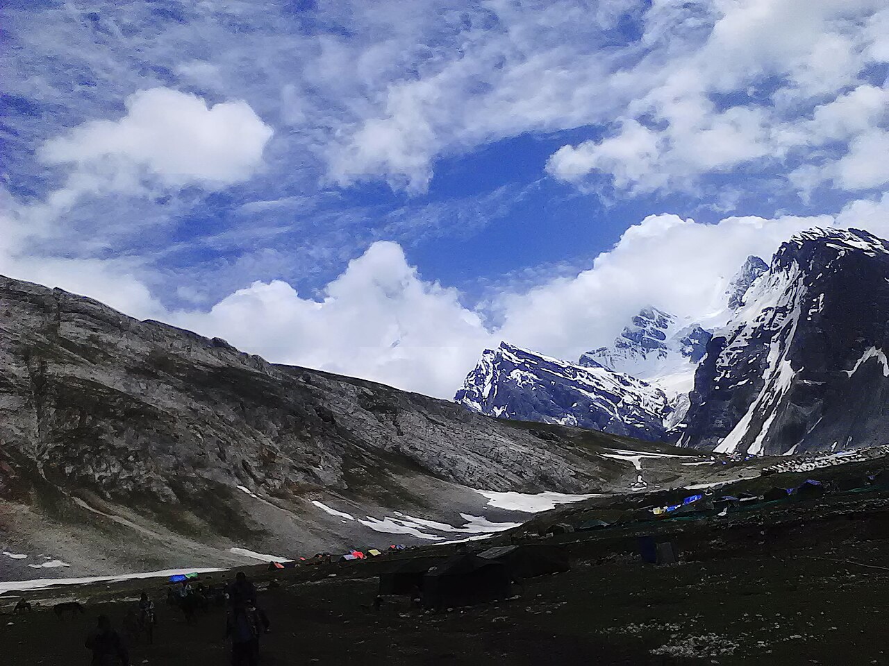 Expansive green valley with pilgrim camps set up against high mountain walls