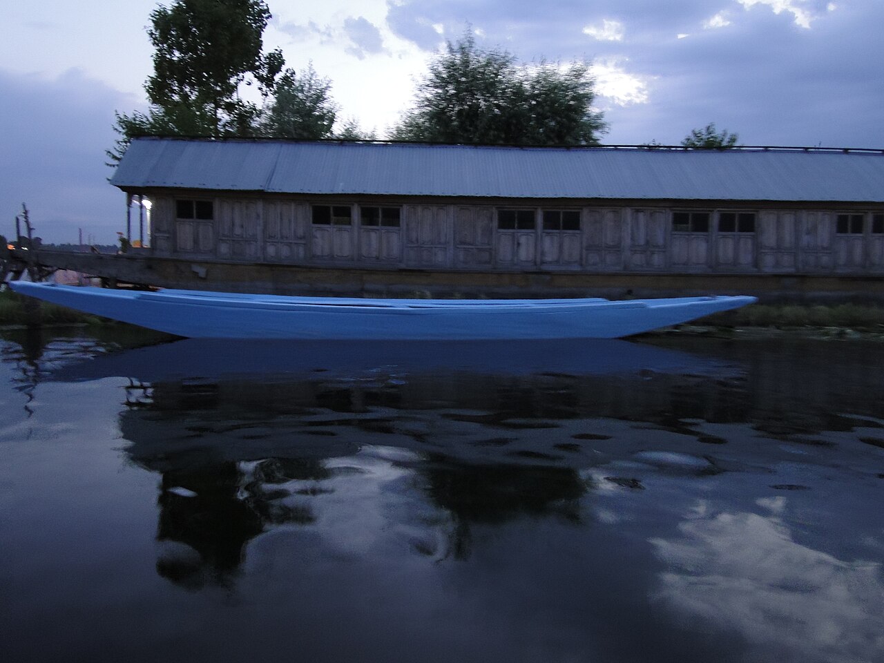 Wooden houseboats moored along the calm shore of Dal Lake at dusk