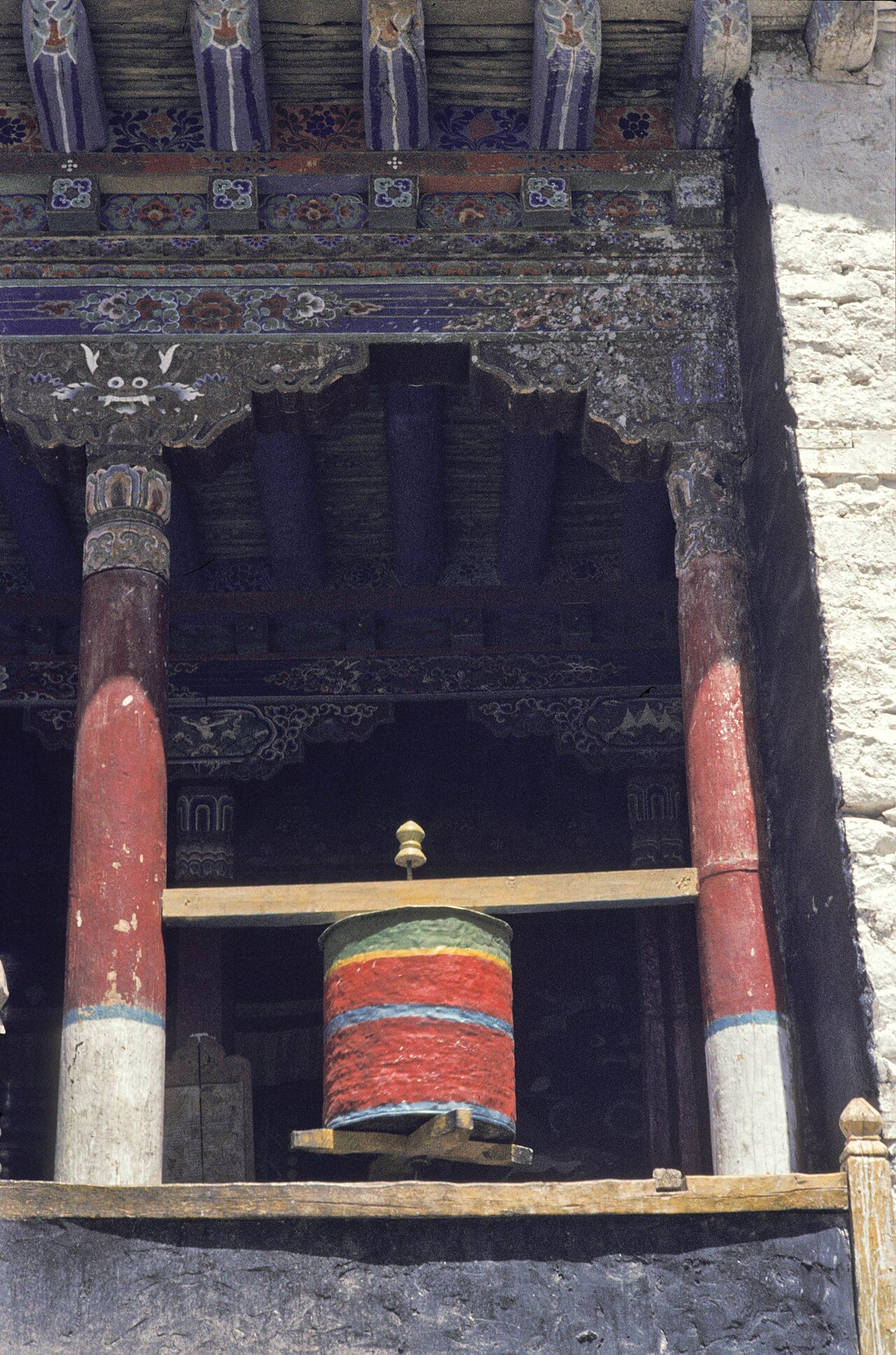 Row of metal prayer wheels along a stone wall in Ladakh