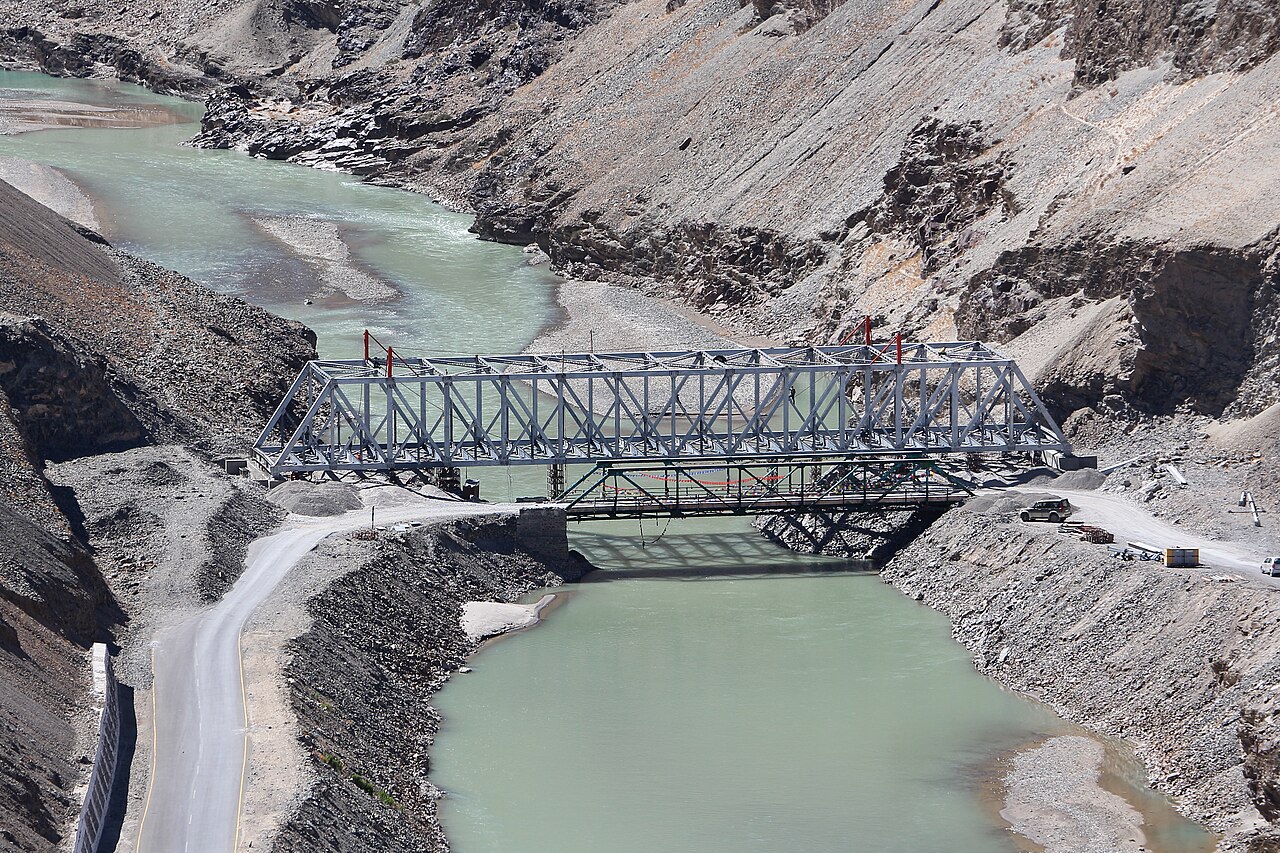 A narrow mountain road running alongside the blue Indus River.