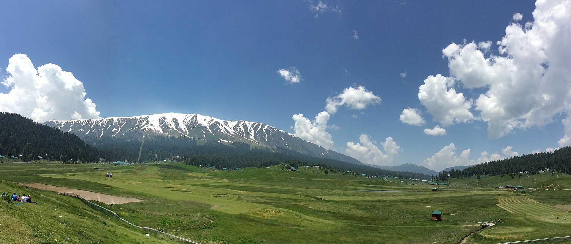 Wide shot of the green Gulmarg meadow with mountains in the background